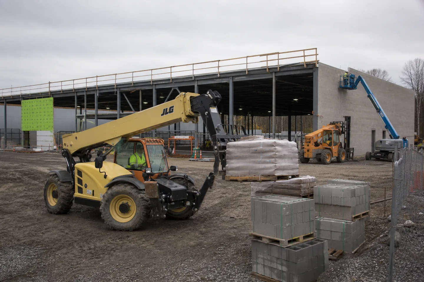 JLG telehandler lifting palletized material on a commercial jobsite with SkyTrak equipment nearby