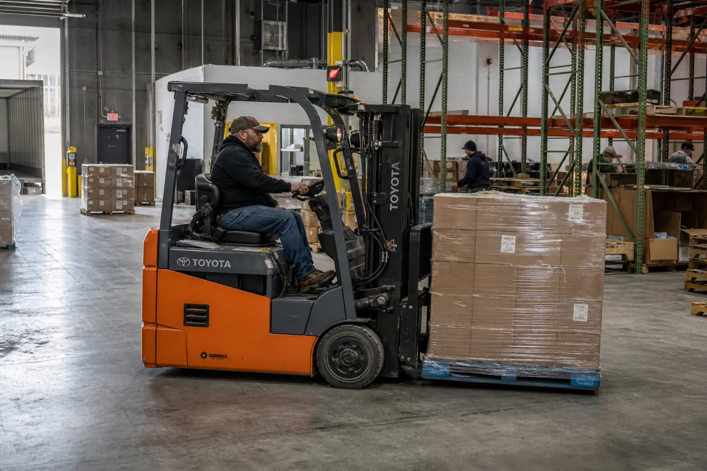 Toyota electric forklift moving palletized inventory in a working warehouse